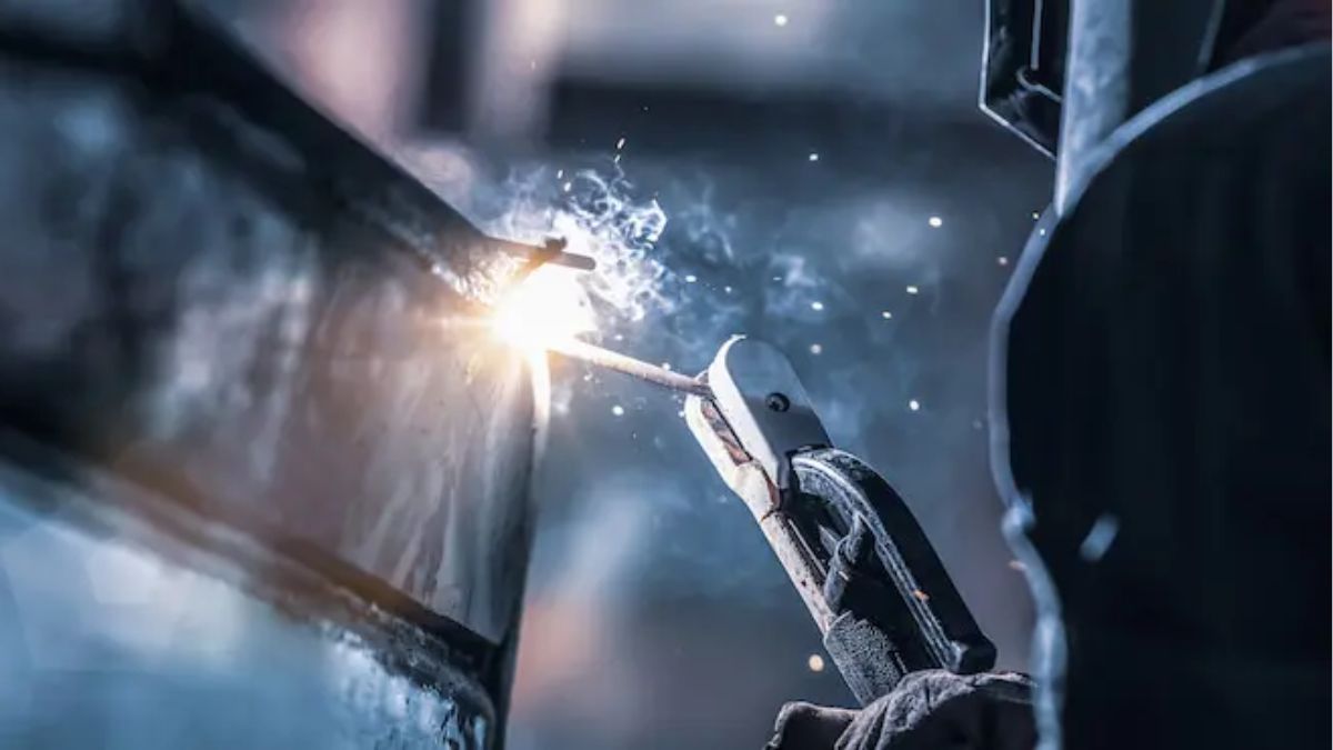 "Thợ hàn que điện tử SMAW đang thực hiện mối hàn trên thép, tạo hồ quang sáng và tia lửa, ứng dụng phổ biến trong gia công cơ khí và xây dựng."