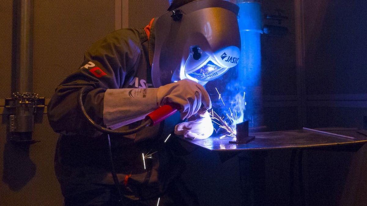 "Thợ hàn hồ quang tay hàn kim loại trong xưởng cơ khí, sử dụng bảo hộ hàn JASIC, tia lửa phát ra trong quá trình hàn."