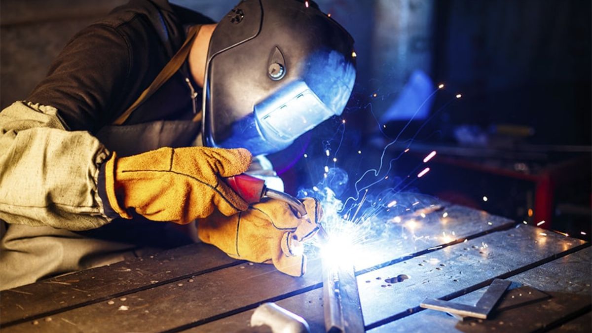 "Thợ hàn hồ quang tay đang hàn kim loại, tia lửa phát ra trong xưởng cơ khí, sử dụng bảo hộ hàn an toàn."